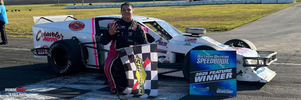 Race car driver celebrating victory by waving a checkered flag beside the car.