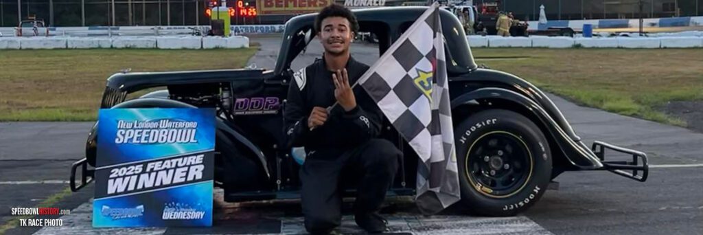 Racing driver celebrating with a checkered flag beside a car.