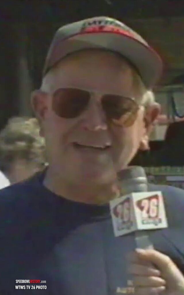 Man wearing sunglasses and cap holding a microphone with a news logo.