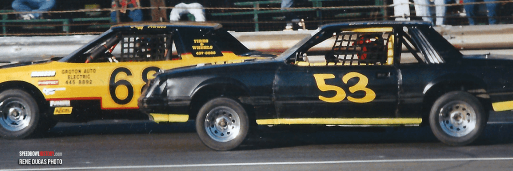Two vintage race cars numbered 6 and 53 side by side on a dirt track.