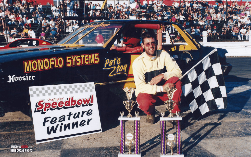 Race car driver celebrating victory with a checkered flag and trophy.