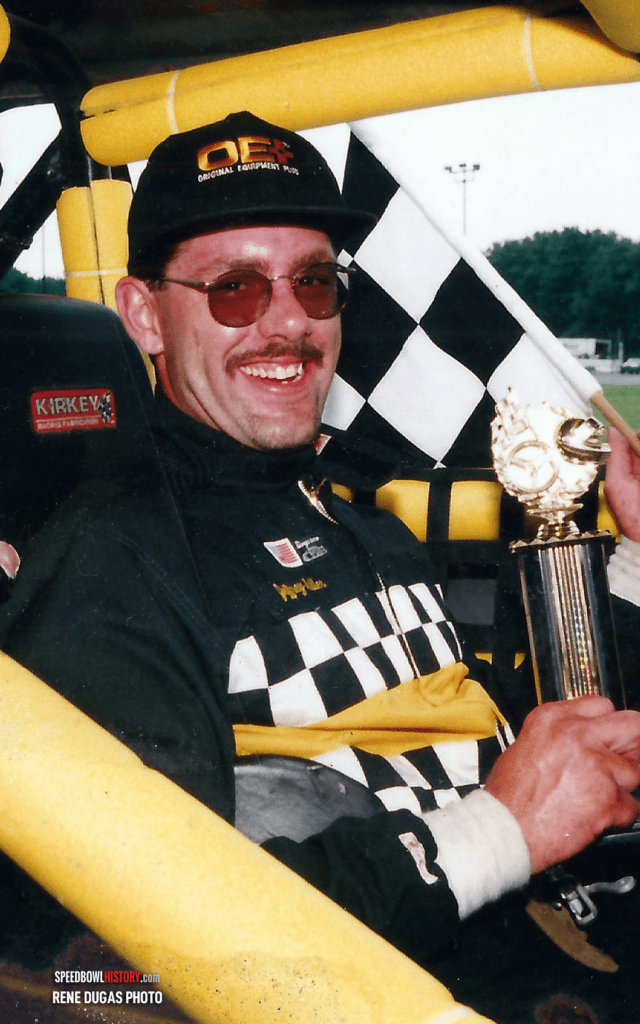 Smiling race car driver holding a trophy inside a race car.
