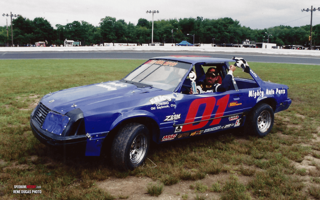 A blue race car numbered 01 on a grassy field.
