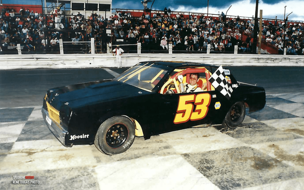 Race car number 53 on the track with crowd in the background.